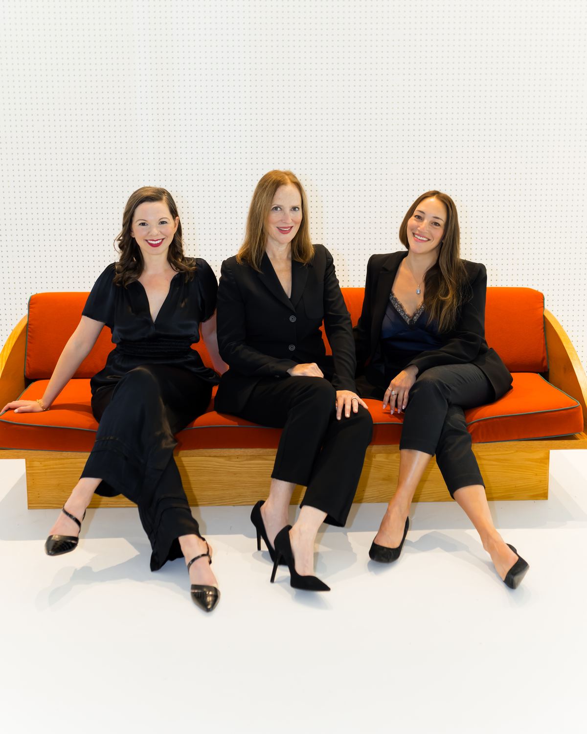 Ashley, Lisa, and Beth of Lisa Clampitt Matchmaking laughing together on an orange sofa